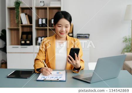 Confident Asian woman with a smile standing holding notepad and tablet at the office. 134542869