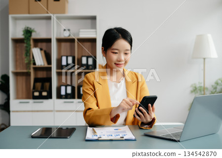 Confident Asian woman with a smile standing holding notepad and tablet at the office. Confident Asian woman with a smile standing holding notepad and tablet at the office. 134542870