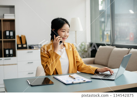 Confident Asian woman with a smile standing holding notepad and tablet at the office. 134542875