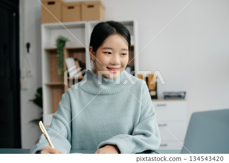 Confident Asian woman with a smile standing holding notepad and tablet at the office. 134543420