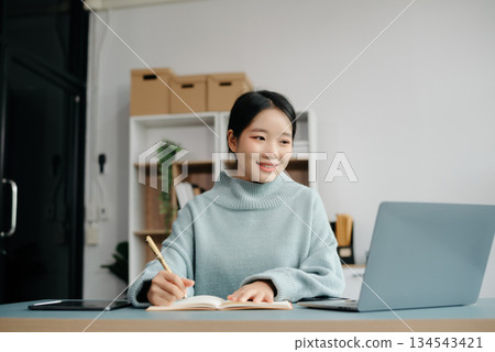 Confident Asian woman with a smile standing holding notepad and tablet at the office. Confident Asian woman with a smile standing holding notepad and tablet at the office. 134543421