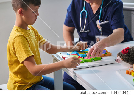 Child engages in interactive play with colorful shapes while receiving guidance from a healthcare professional in a bright room Child engages in interactive play with colorful shapes while receiving guidance from a healthcare professional in a bright room 134543441