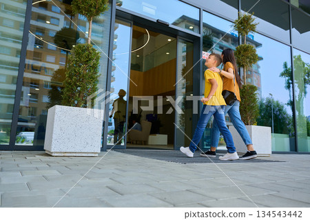 Family enjoys a sunny day while walking into a modern building with children in casual outfits Family enjoys a sunny day while walking into a modern building with children in casual outfits 134543442