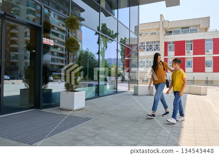 Mother and son walk towards a modern building in a city on a sunny day 134543448