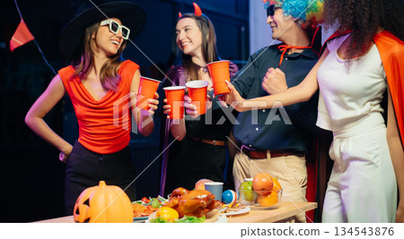 Halloween party with friends in costumes, enjoying drinks, food, and festive decorations. Perfect for autumn gatherings Halloween party with friends in costumes, enjoying drinks, food, and festive decorations. Perfect for autumn gatherings 134543876