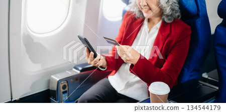 Asian seniorexecutive excels in first class, multitasking with digital tablet, laptop and smartphone. Travel in style, Asian seniorexecutive excels in first class, multitasking with digital tablet, laptop and smartphone. Travel in style, 134544179