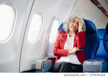 senior woman sitting on an airplane with her head in her hands. Asian woman sitting in a seat in airplane 134544182