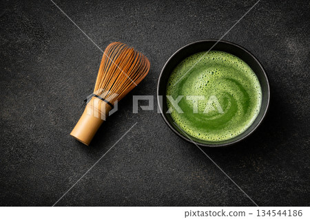 Aerial view of a swirl pattern of matcha and a bamboo whisk on a black stone background 134544186
