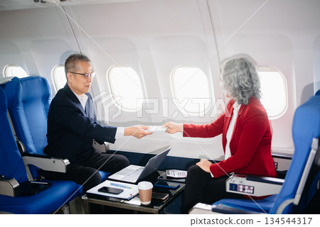 Business meeting in airplane, asian Mature businessman in private jet is talking with Mature female colleague and documents, business people flying 134544317