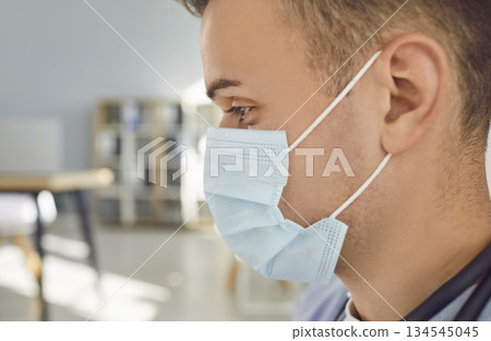 Close up portrait of pensive man doctor or nurse in blue face mask standing in office. Close up portrait of pensive man doctor or nurse in blue face mask standing in office. 134545045