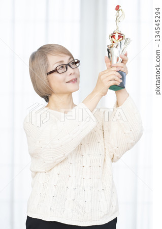 一位笑容滿面的老婦人手捧獎杯 一位笑容滿面的老婦人手捧獎杯 134545294