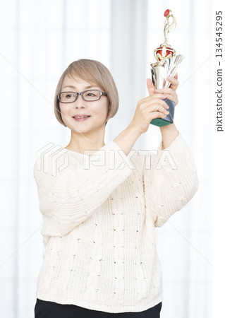 一位笑容滿面的老婦人手捧獎杯 一位笑容滿面的老婦人手捧獎杯 134545295