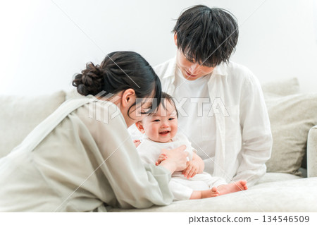 一個年輕的家庭在家裡的客廳沙發上和他們的寶寶一起玩耍。 134546509