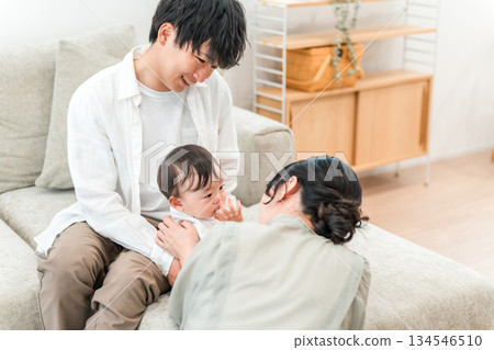 一個年輕的家庭在家裡的客廳沙發上和他們的寶寶一起玩耍。 一個年輕的家庭在家裡的客廳沙發上和他們的寶寶一起玩耍。 134546510