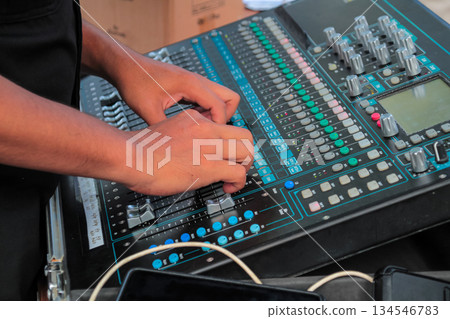 Sound engineer adjusting digital faders on a multi-channel audio mixing board during a live performance setup. Sound engineer adjusting digital faders on a multi-channel audio mixing board during a live performance setup. 134546783