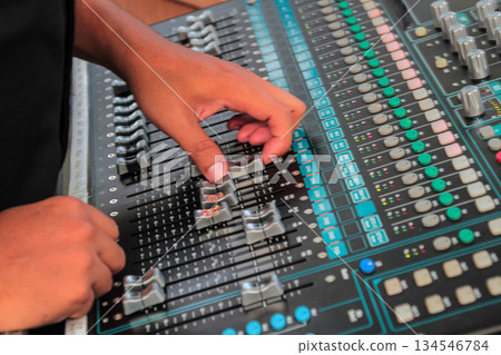Closeup shot of sound engineer adjusting faders on a black audio mixing board during a live event or recording session. Closeup shot of sound engineer adjusting faders on a black audio mixing board during a live event or recording session. 134546784