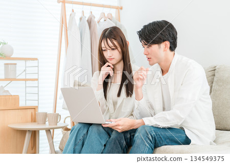 A young Asian couple sitting on the sofa in the living room at home looking at a computer and looking troubled A young Asian couple sitting on the sofa in the living room at home looking at a computer and looking troubled 134549375