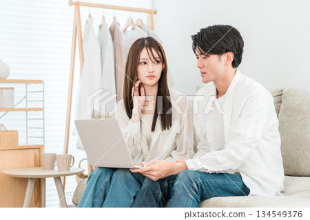 A young Asian couple sitting on the sofa in the living room at home looking at a computer and looking troubled A young Asian couple sitting on the sofa in the living room at home looking at a computer and looking troubled 134549376