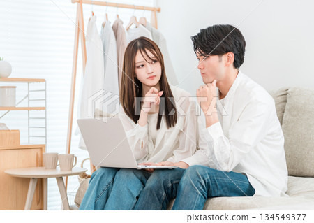 A young Asian couple sitting on the sofa in the living room at home looking at a computer and looking troubled A young Asian couple sitting on the sofa in the living room at home looking at a computer and looking troubled 134549377