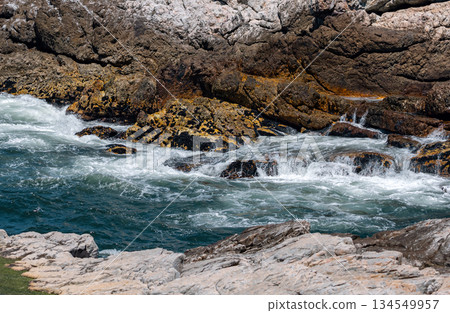 Waves crashing against rocky shore under clear blue sky, ocean coastal landscape 134549957