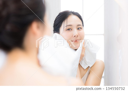 一位女士用Oru保濕保養品洗臉後對著鏡子看東西。 134550732