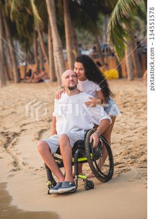 Disabled man in a wheelchair with his wife on the beach. Disabled man in a wheelchair with his wife on the beach. 134551578