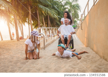 Disabled man in a wheelchair moves on a ramp to the beach with his family. 134551586