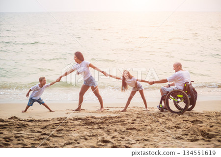 Disabled man in a wheelchair with his family on the beach. Disabled man in a wheelchair with his family on the beach. 134551619