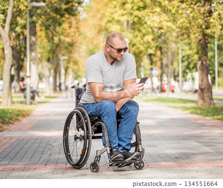 Handicapped man in wheelchair at the park alley use a smartphone 134551664
