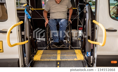 A man in a wheelchair on a lift of a vehicle for people with disabilities A man in a wheelchair on a lift of a vehicle for people with disabilities 134551668