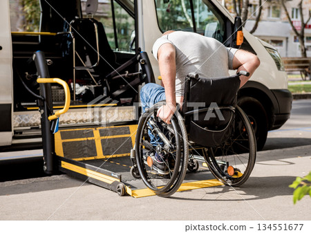 A man in a wheelchair moves to the lift of a specialized vehicle A man in a wheelchair moves to the lift of a specialized vehicle 134551677