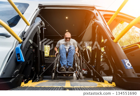 A man in a wheelchair on a lift of a vehicle for people with disabilities A man in a wheelchair on a lift of a vehicle for people with disabilities 134551690