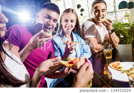 Cheerful friends in the pub. Drinking beer, eating pizza, talking, having fun. Cheerful friends in the pub. Drinking beer, eating pizza, talking, having fun. 134552024