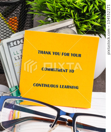 A vivid yellow note displaying appreciation for continuous learning rests on a desk, next to United States Dollars. Eyeglasses and a plant subtly accent the scene A vivid yellow note displaying appreciation for continuous learning rests on a desk, next to United States Dollars. Eyeglasses and a plant subtly accent the scene 134552171