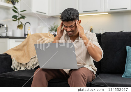 Indian man squints at laptop screen rubs temples does breath exercise then returns to focused work Indian man squints at laptop screen rubs temples does breath exercise then returns to focused work 134552957