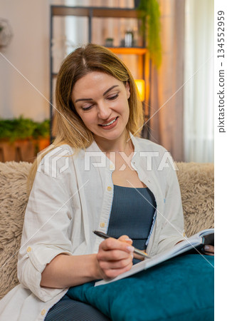 Adult woman sketching in notebook at home, thoughtful and inspired mood with creative expression 134552959