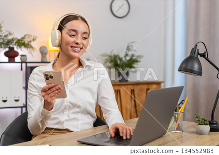 Young happy businesswoman plays soft music on smartphone relax chill taking a break returns to tasks 134552983