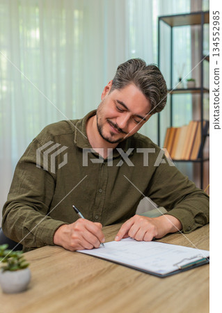 Middle-aged man satisfied signs documents approving content signing paperwork gladly at table desk Middle-aged man satisfied signs documents approving content signing paperwork gladly at table desk 134552985