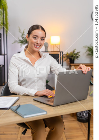 Young businesswoman opens laptop smiles starts typing and begins fresh workday with focus and energy Young businesswoman opens laptop smiles starts typing and begins fresh workday with focus and energy 134552995