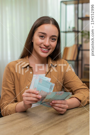 Young woman counting money hryvnia cash satisfied with salary earnings celebrating financial success Young woman counting money hryvnia cash satisfied with salary earnings celebrating financial success 134552996