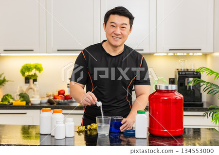 Sportsman pours supplement powder into glass of water in kitchen at home for daily fitness energy up 134553000