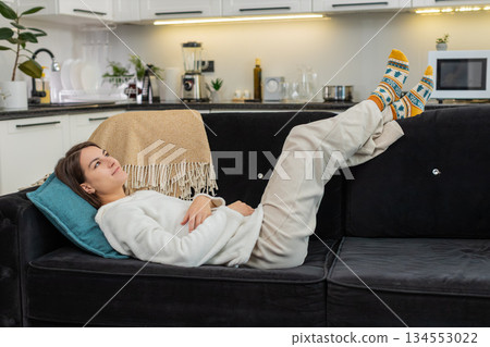 Young woman relaxes indoors feet up enjoys comfort smiles with quiet climate control air and soft Young woman relaxes indoors feet up enjoys comfort smiles with quiet climate control air and soft 134553022