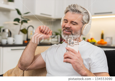 Middle-aged man turns on playlist in headphones nods to beat smiles relax takes break from work calm 134553090