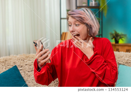 Young woman celebrating victory in online mobile game, expressing excited surprise joyful emotions Young woman celebrating victory in online mobile game, expressing excited surprise joyful emotions 134553124
