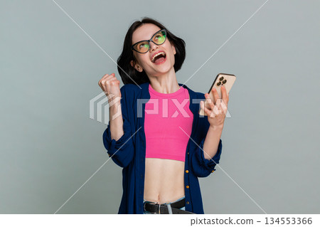 Woman looking at smartphone smiling joyfully raising hand celebrating online victory lottery win 134553366