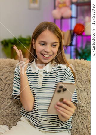 Child girl kid playing mobile game app on smartphone at home, smiling and celebrating happy victory 134553380