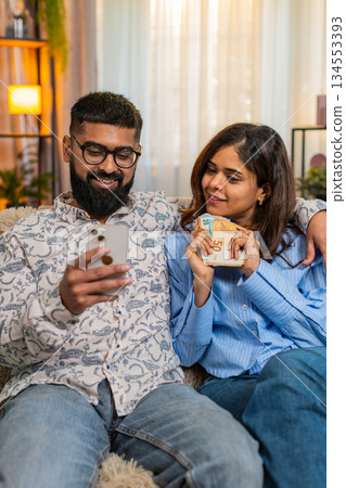Indian family couple man woman planning expenses with cash and smartphone discussing shopping salary 134553393