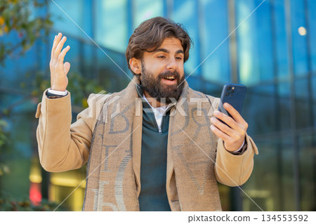 Happy Indian man using smartphone celebrating victory win good message news on downtown city street Happy Indian man using smartphone celebrating victory win good message news on downtown city street 134553592