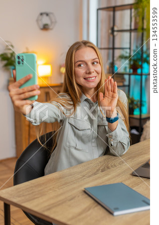 Caucasian mature woman freelancer using smartphone having video call smiling while sitting at table 134553599