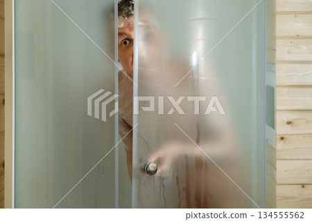 Person peeking through a shower door with steam covering the glass in a bathroom setting 134555562